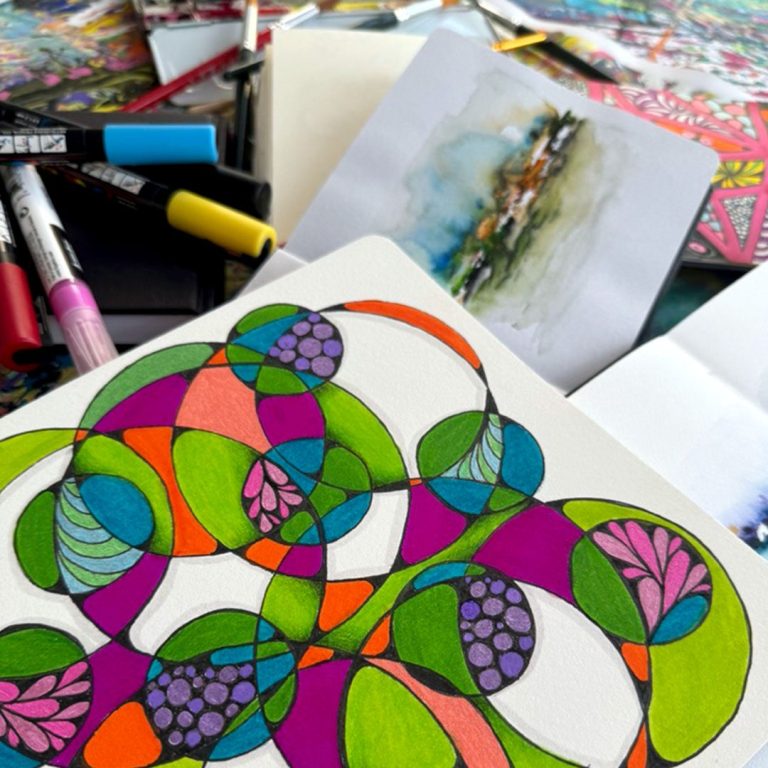 Offenes Altelier Ein Skizzenbuch mit einem bunten Motiv aus runden Formen und Stiften im Hintergrund