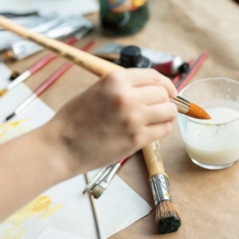 Hand hält einen Pinsel über einen Glasbecher