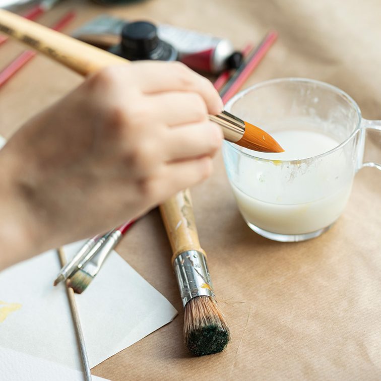 Hand mit Pinsel über ein Glasbecher